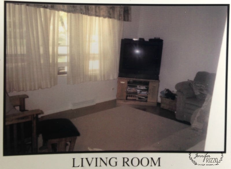 A living room with a large window with curtains, a television on a stand in the corner, a couch, a chair, and a carpeted floor featuring money-saving home decorating ideas for stylish comfort.