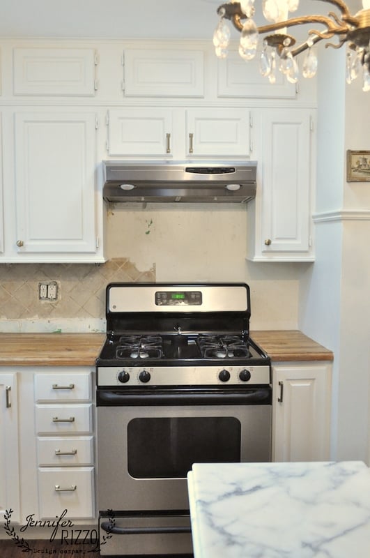 A stainless steel gas stove with an overhead range hood is set between white cabinets, a light wood countertop, and classic kitchen subway tile in a modern kitchen.
