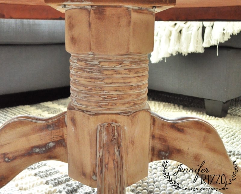 A close-up of a wood coffee table with white wax shows its distressed, rustic finish. A gray sofa and patterned rug are visible in the background. The image includes the Jennifer Rizzo logo.
