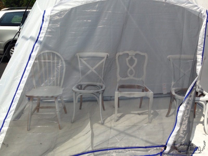 Four different white chairs are arranged in a row inside a tent with a transparent plastic cover, perfect for spray painting chairs to make a matched set.