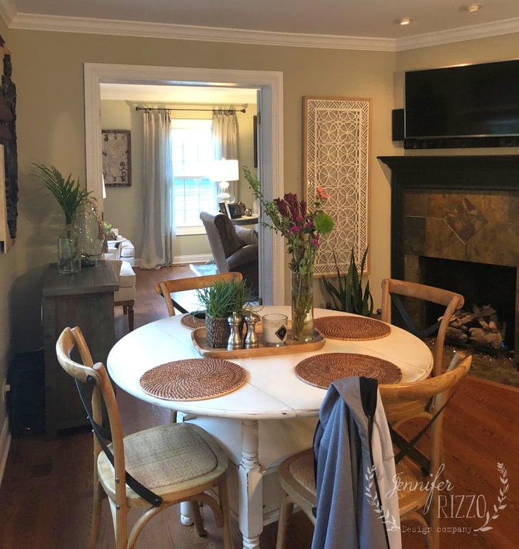 A round white dining table, refreshed with a painted kitchen table makeover, pairs with four wooden chairs in a cozy room with hardwood floors, near a fireplace and a living area in the background.