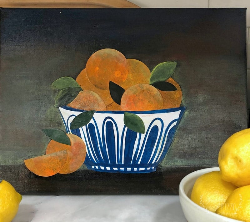 A painting of a blue and white bowl filled with oranges and leaves, reminiscent of cut paper still life wall art. A sliced orange lies beside the bowl, while lemons adorn the foreground against a dark background.