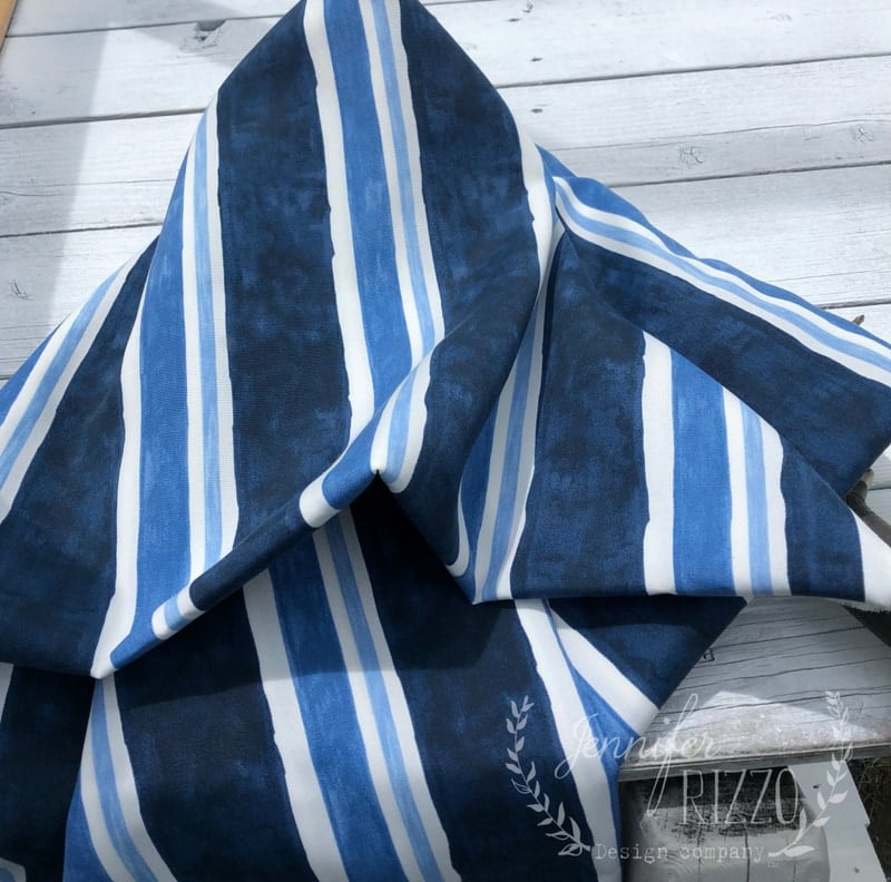 A piece of fabric with bold blue, white, and black stripes, perfect as a new fabric canopy for a playset, is draped on a white wooden surface.