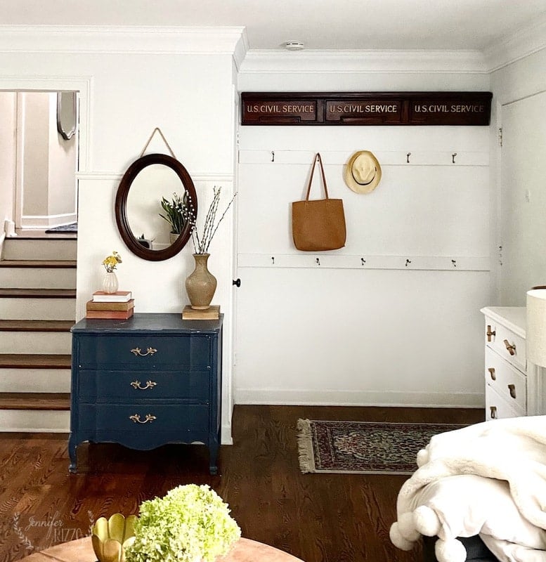 A hallway with a blue chest, mirror, decorative vase, and hooks holding a hat and bag sits beneath "U.S. Civil Service" signs—finished with fast and easy crown molding for a polished look.