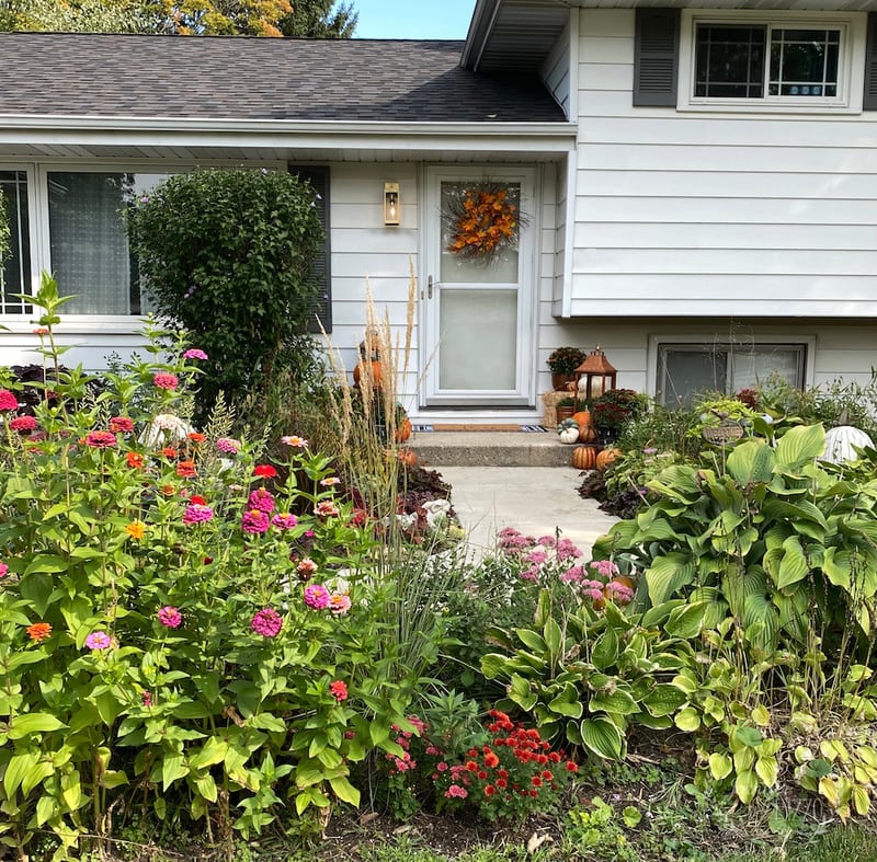 Festive fall front porch with pumpkins, wreath, and colorful flowers.