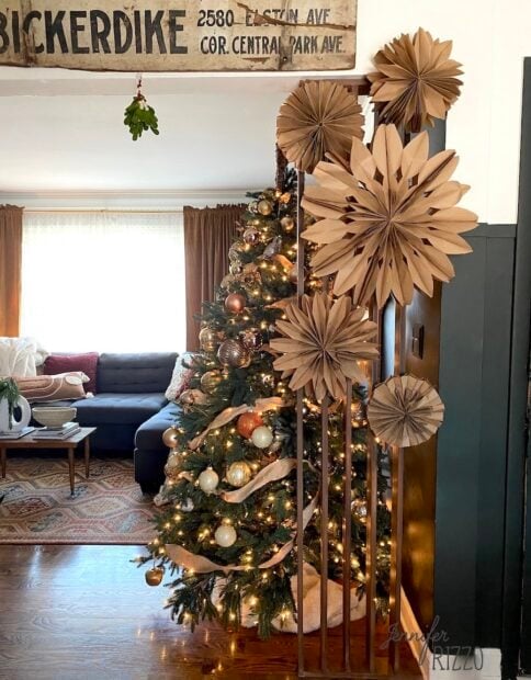 DIY paperbag snowflakes from lunch bags on a wood slat wall next to a Christmas tree under a vintage sign