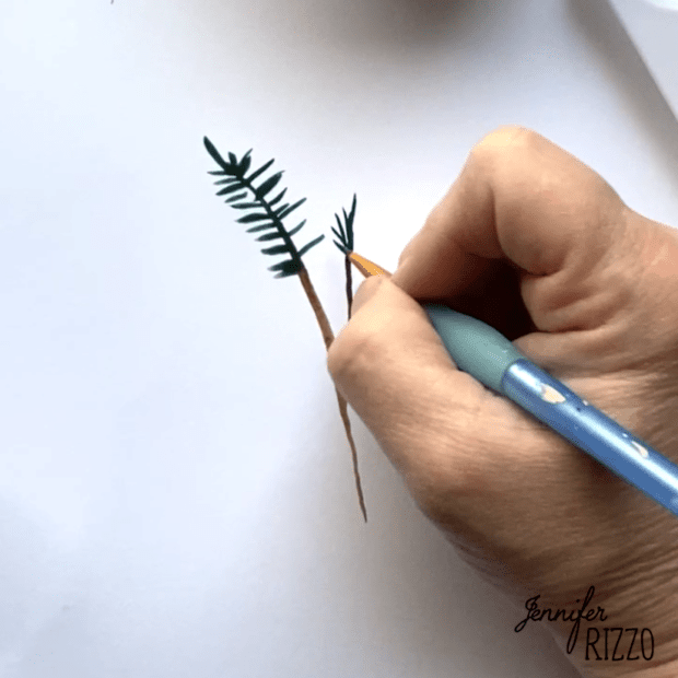 A hand uses a blue pen to sketch green pine needles and brown branches on white paper, painting a watercolor pine tree branch with delicate detail.