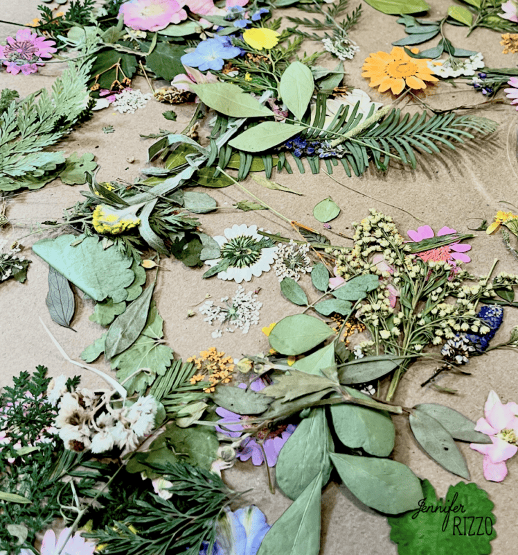 Assorted dried leaves, flowers, and greenery are scattered on a brown surface, displaying a variety of textures and colors—perfect materials to make a framed dried flower vintage photo collage.