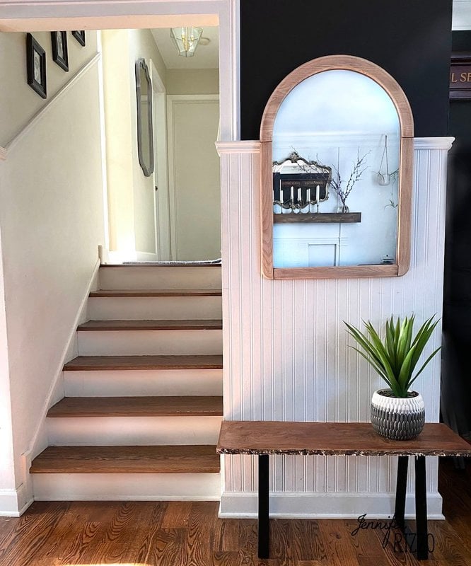 Live edge bench in a front entry with an arched mirror and plant on a white wall enct to stairs