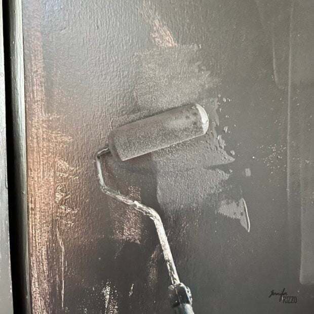 A paint roller is being used to apply dark gray paint, ideal for painting interior bedroom doors black, to a smooth, flat surface.