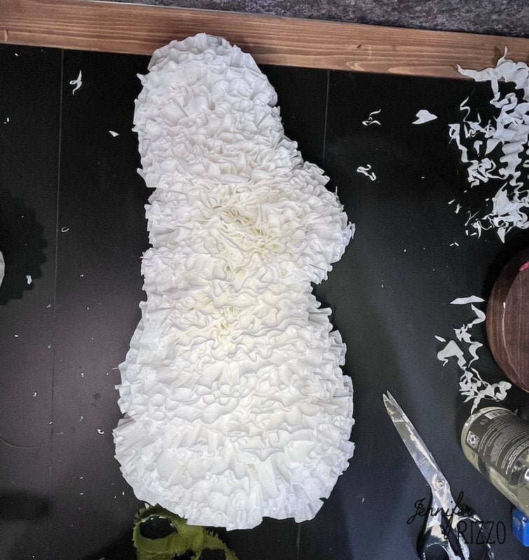 A white, textured, ruffled paper snowman shape is laid out on a black surface, with crafting tools and paper scraps nearby—a playful scene reminiscent of a Fun Coffee Filter Easter Bunny Craft.