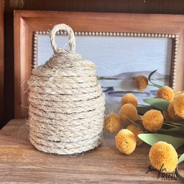 DIY bee skep made from rope and cardboard in front of a landscape and yellow flowers