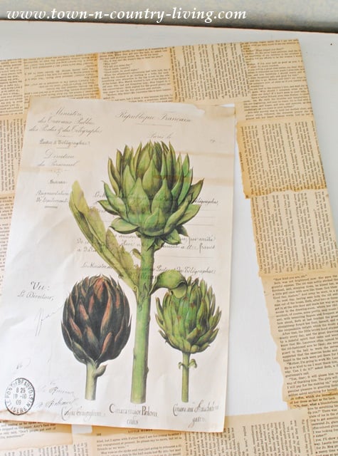 A vintage DIY botanical art illustration of artichokes is displayed on top of a background made of layered, torn book pages.