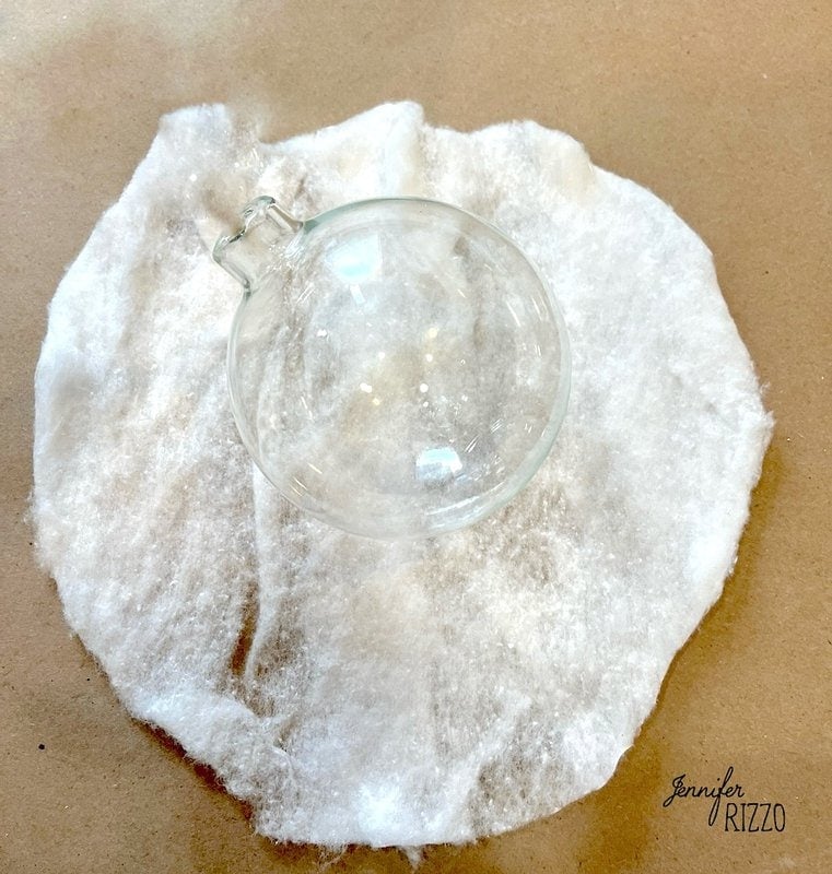 A clear glass ornament sits on a layer of fluffy cotton on a beige surface.