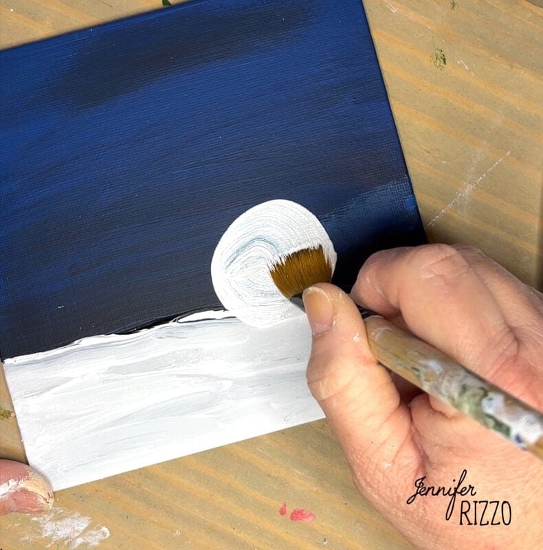 A hand painting a blue and white abstract artwork on a square canvas, with a signature reading "Jennifer Rizzo" in the corner.