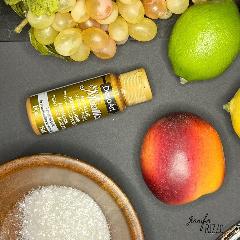 Acrylic paint bottle, grapes, lime, nectarine, and a wooden bowl with salt on a dark surface.