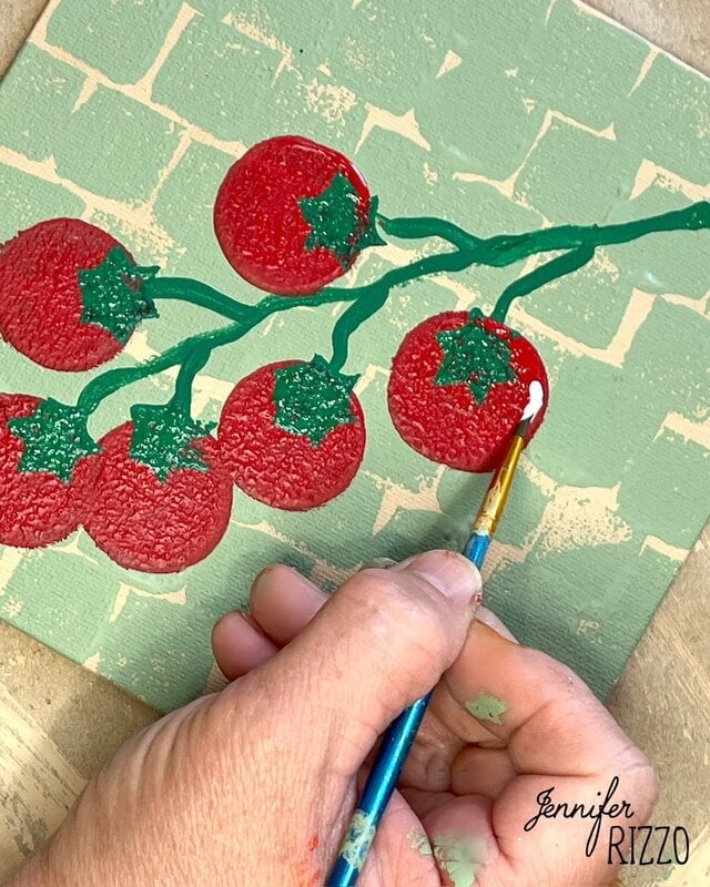 A hand is painting red tomatoes on green vines on a textured canvas with a paintbrush. The signature "Jennifer Rizzo" appears in the bottom right corner.