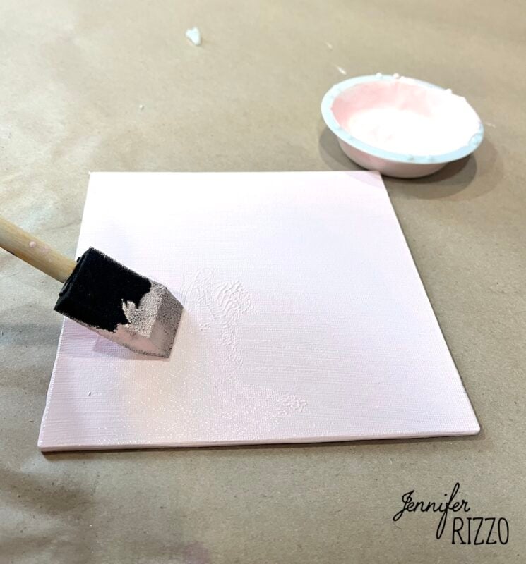 A foam brush applies light pink paint to a small square canvas, with a dish of paint nearby. The name "Jennifer Rizzo" is written in the bottom right corner.