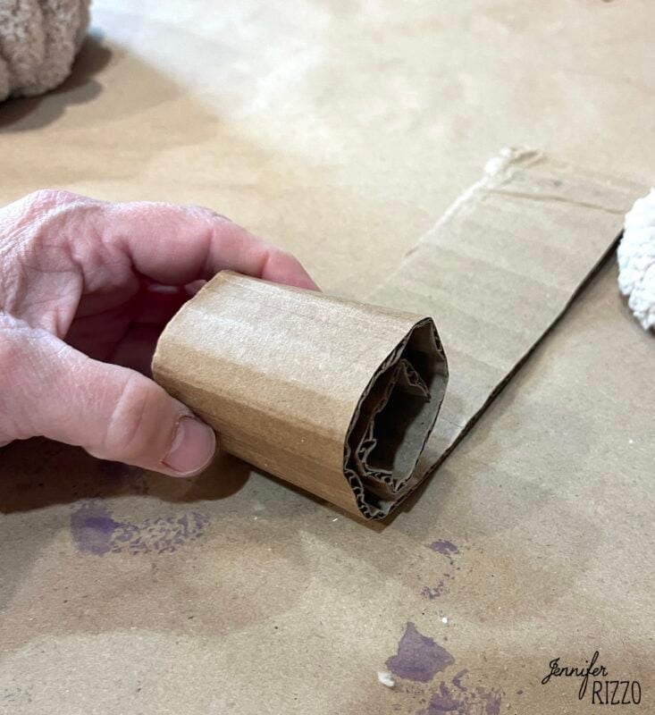 A hand holds a rolled piece of corrugated cardboard on a brown surface.