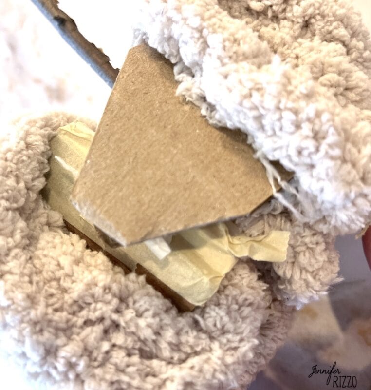 A close-up of a piece of cardboard with masking tape, partially wrapped in textured, fluffy white fabric.