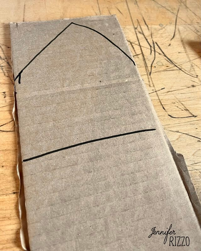 A rectangular piece of cardboard with a hand-drawn house outline in black marker.