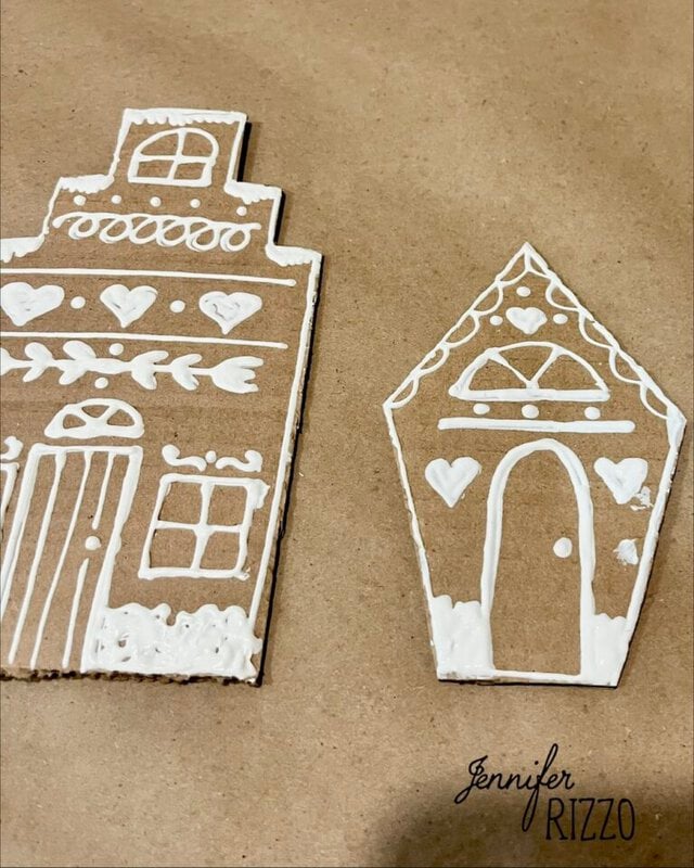 Two cardboard house cutouts decorated with white icing in patterns of windows, doors, and hearts.