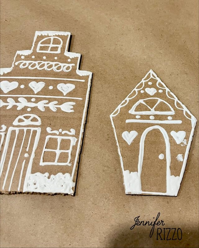 Two cardboard house cutouts decorated with white icing in patterns of windows, doors, and hearts.