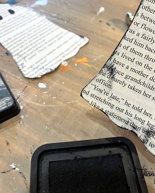 A closeup of paper pieces with printed text, an ink pad, and some paint splatters on a tabletop workspace.