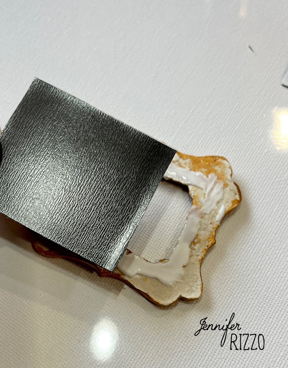 A piece of black adhesive vinyl is being applied to a vintage-style metal label holder with glue on a white surface.