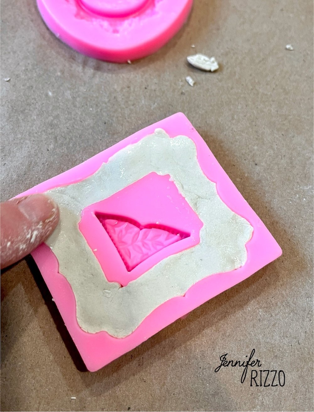 A hand presses white clay into a pink silicone mold with a butterfly design on a brown surface.