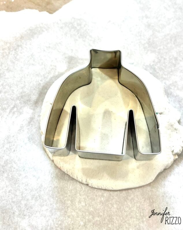 Sweater-shaped cookie cutter pressed into white dough on a piece of parchment paper.