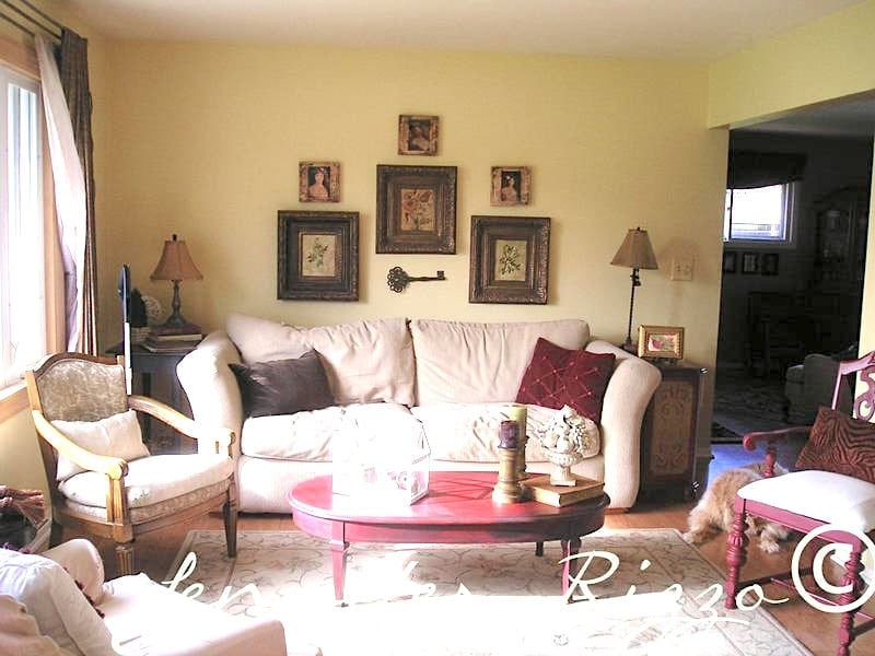 A living room with a cream-colored sofa, framed art on the wall, a red coffee table, two armchairs, and table lamps on either side of the sofa.