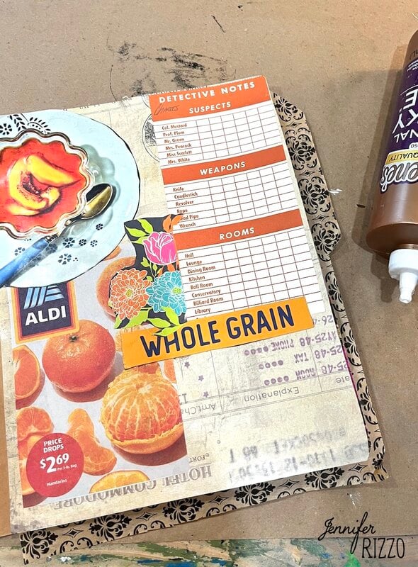 A scrapbook page featuring a Clue-inspired detective notes sheet, fruit images, a "Whole Grain" label, floral stickers, and a bottle of crafting glue on the side.