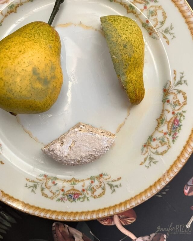 A pear and a wedge of soft white cheese are arranged on a decorative porcelain plate with floral patterns.
