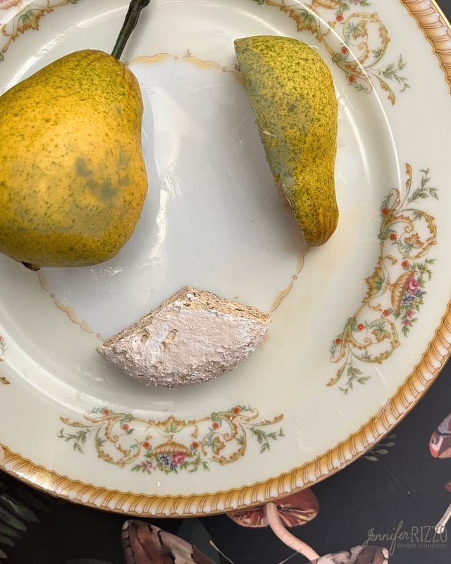 A pear and a wedge of soft white cheese are arranged on a decorative porcelain plate with floral patterns.