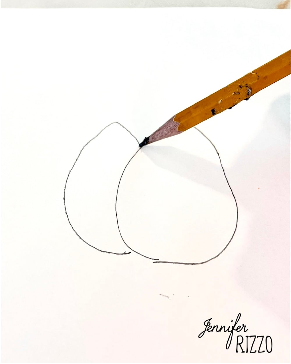 A pencil draws two overlapping oval shapes on white paper, creating the outline of a simple sketch.