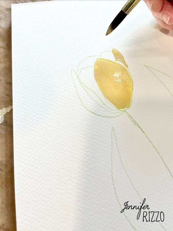 A hand uses a paintbrush to apply yellow watercolor to a flower sketch on textured white paper. The name "Jennifer Rizzo" appears in the corner.