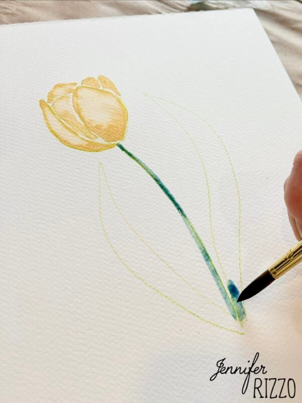 A hand paints a yellow tulip with green stem and leaves on white paper using watercolors. The name "Jennifer Rizzo" is written in the bottom right corner.