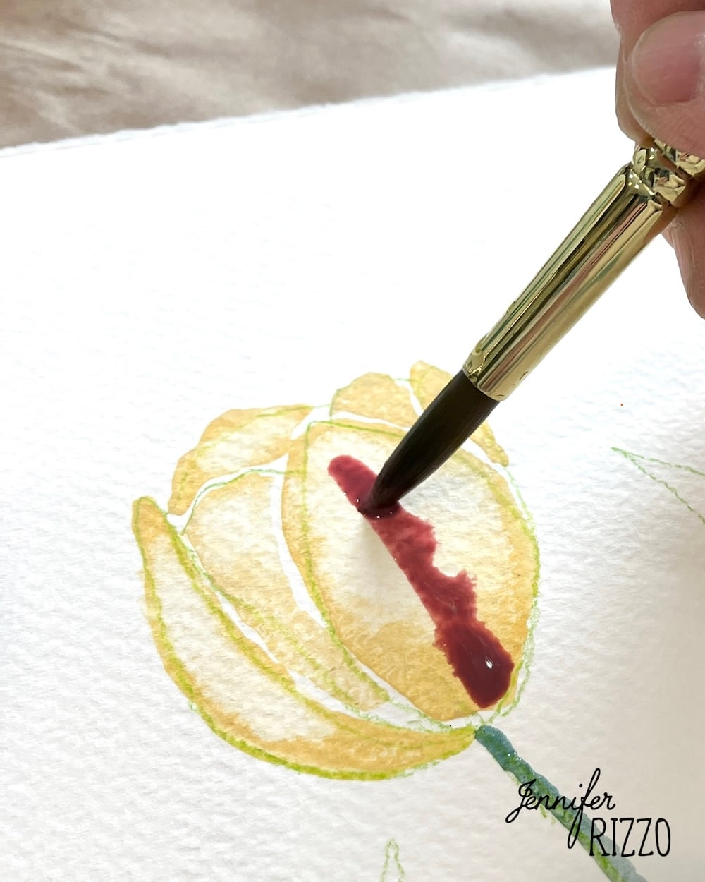 A hand uses a paintbrush to add red watercolor paint to a yellow flower illustration on textured paper.