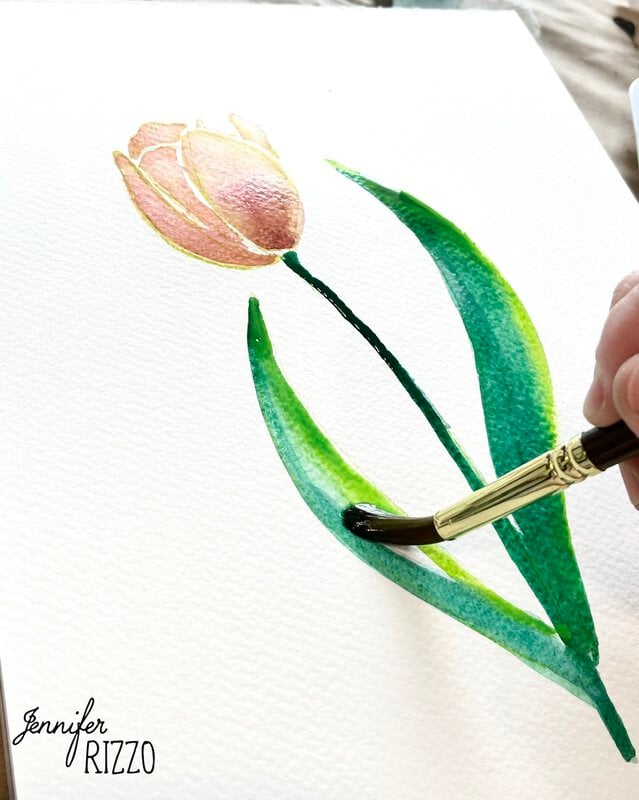 A hand uses a paintbrush to paint green leaves on a watercolor tulip on white paper. The name "Jennifer Rizzo" is printed in the lower left corner.