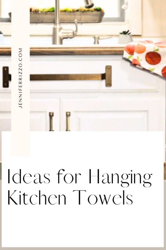 A white kitchen cabinet with a towel bar mounted on the front holds a kitchen towel under the countertop next to a sink. Text reads: “Ideas for Hanging Kitchen Towels” – the perfect inspiration for stylish and practical towel storage.