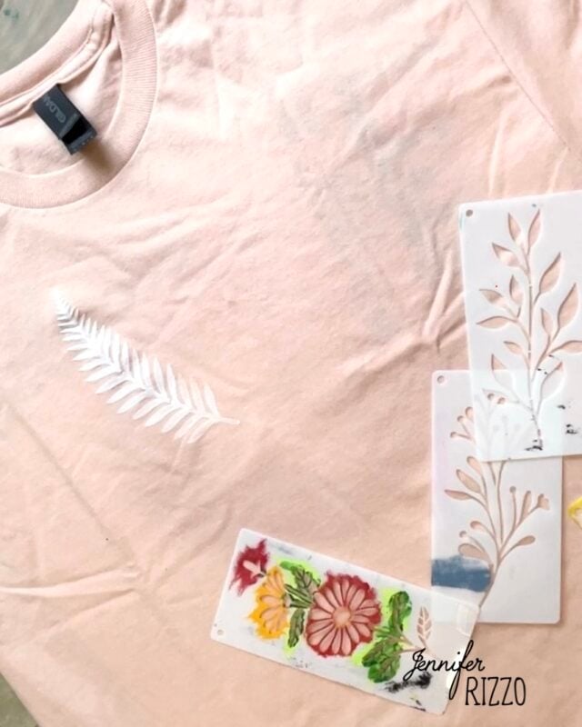 A light pink t-shirt with a white stenciled leaf design, created using Batik with Glue and Stencils, is shown next to several floral and leaf pattern stencils.