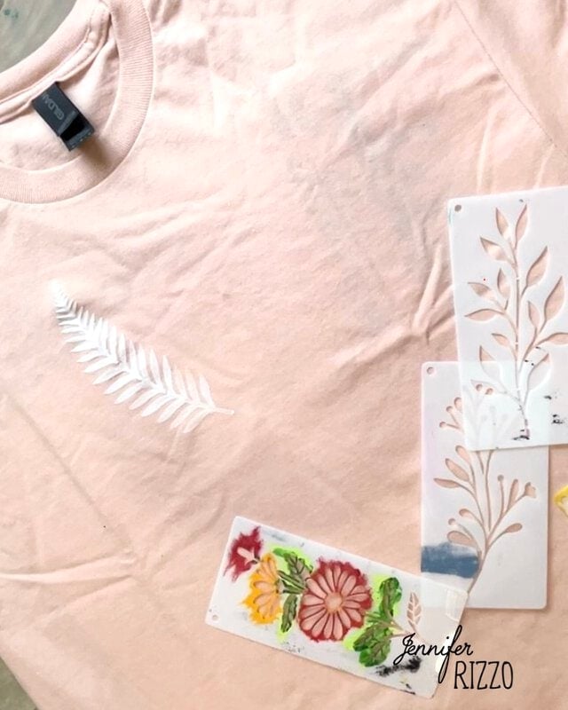 A light pink t-shirt with a white stenciled leaf design, created using Batik with Glue and Stencils, is shown next to several floral and leaf pattern stencils.