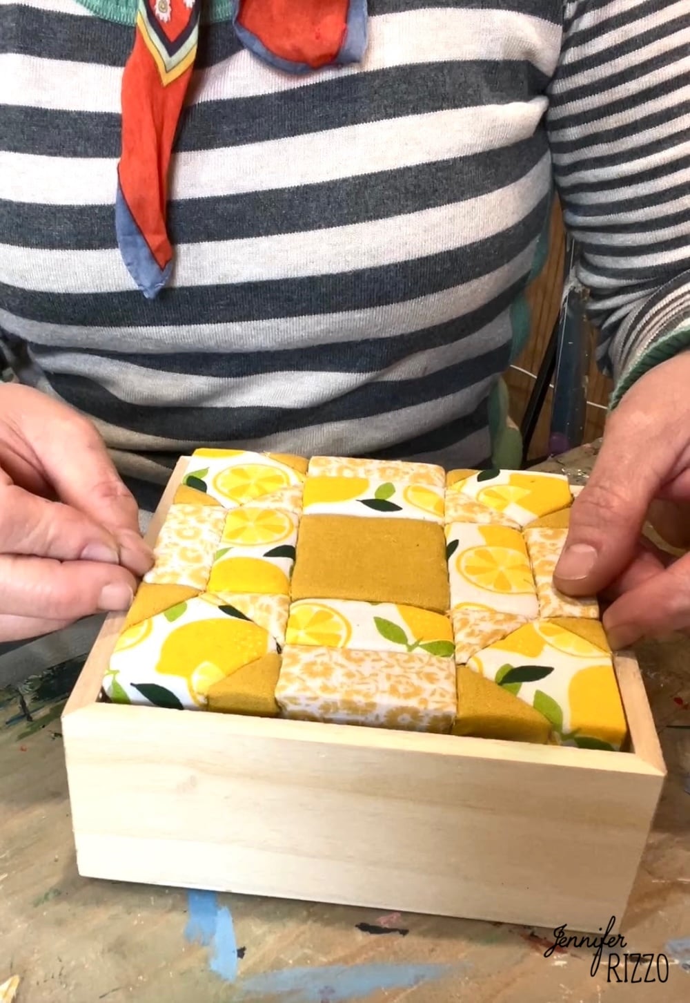 Person assembling a wooden box with a padded, quilted top featuring yellow, white, and lemon-patterned fabric squares using Easy Kinusaiga Art techniques.