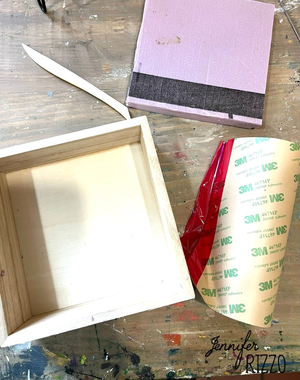 A wooden box, a piece of pink foam with black tape, and a sheet of 3M adhesive film rest on a crafting table—perfect supplies for Easy Kinusaiga Art—featuring the "Jennifer Rizzo" watermark.