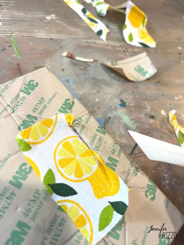 A close-up of cut pieces of adhesive-backed fabric with a lemon pattern on a craft table, perfect for Easy Kinusaiga Art, surrounded by scraps and crafting tools.