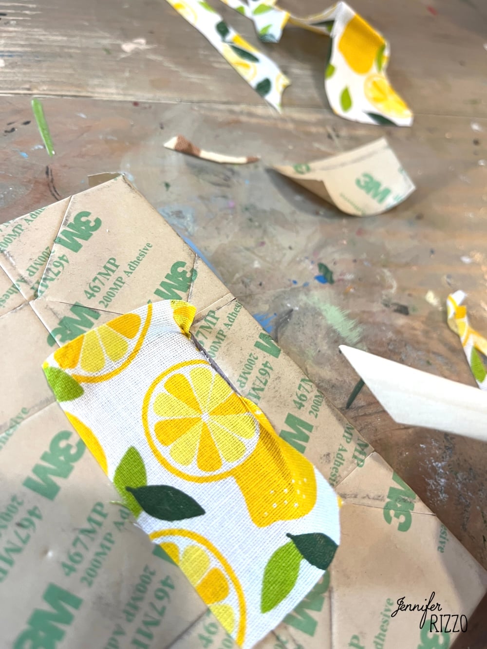 A close-up of cut pieces of adhesive-backed fabric with a lemon pattern on a craft table, perfect for Easy Kinusaiga Art, surrounded by scraps and crafting tools.