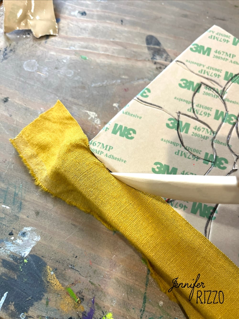 A piece of yellow fabric is being wrapped around a white object on a work surface, featuring Easy Kinusaiga Art techniques, with a sheet of 3M adhesive and scattered art supplies nearby.