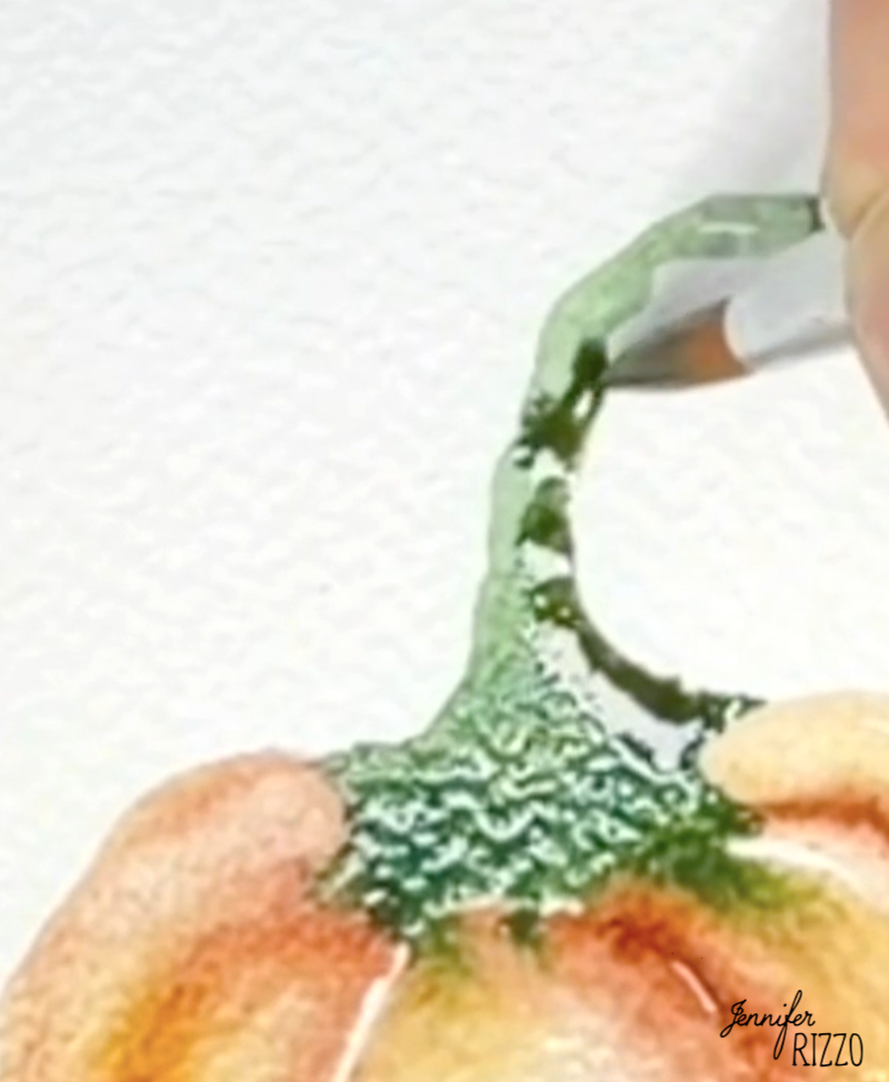 A paintbrush colors the green stem of a watercolor pumpkin on textured paper.