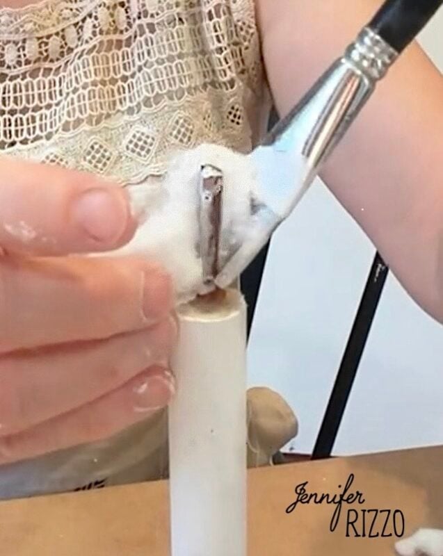 A person applies white paint to a small cylindrical object using a brush, with cotton in hand.
